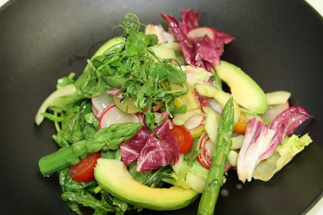 Nahaufnahme eines bunten Salats mit Radieschen, Tomaten, Avocado und grünem Spargel.