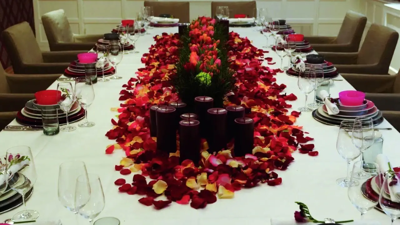 Ein festlich gedeckter Tisch in einem Veranstaltungsraum in Stuttgart, geschmückt mit roten und gelben Rosenblättern, Kerzen und Blumenarrangements in der Mitte.