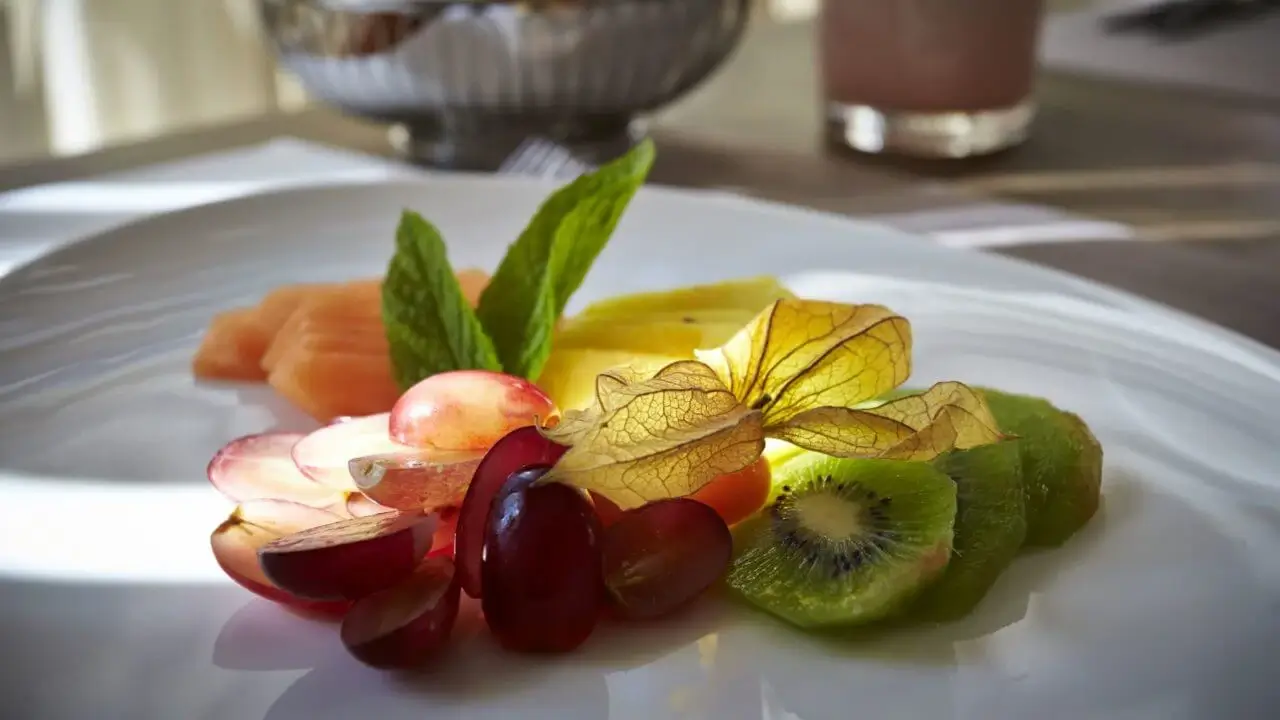 Ein Teller mit frischem Obst, darunter Trauben, Kiwi, Ananas und Melone, garniert mit Minzblättern und einer Physalis.