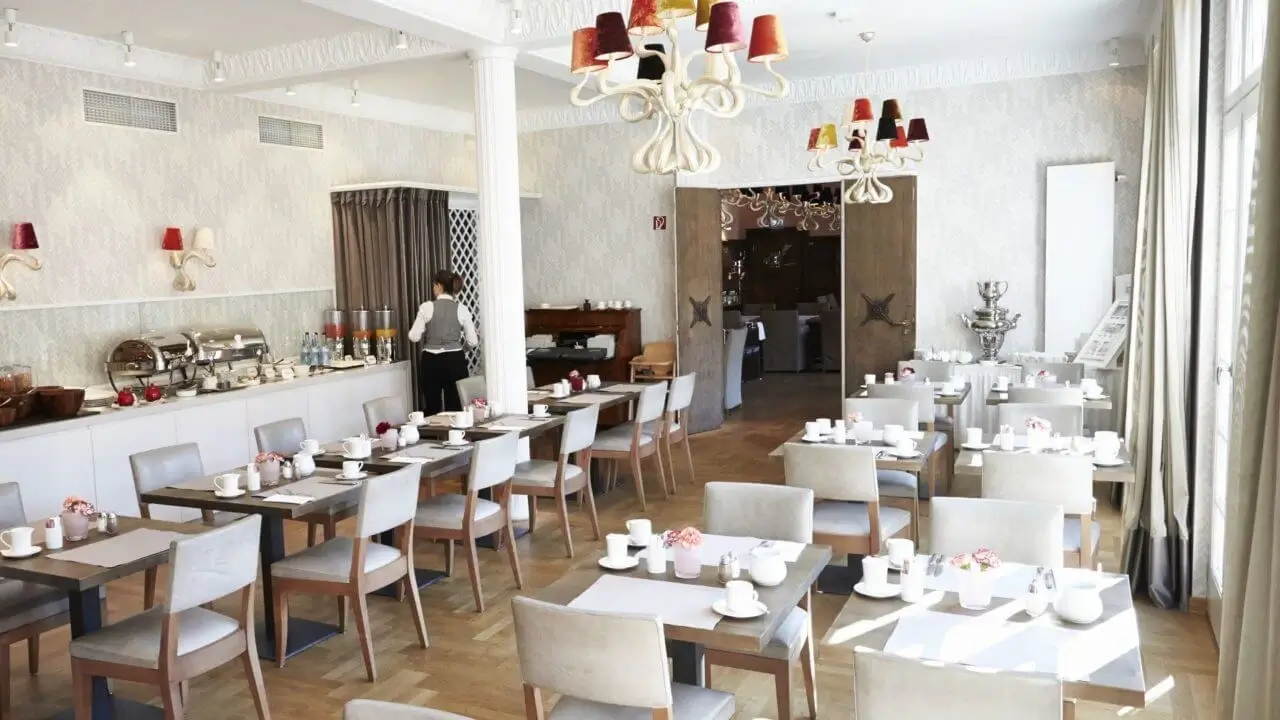 Ein helles, stilvoll eingerichtetes Frühstücksrestaurant mit gedeckten Tischen und Buffet.