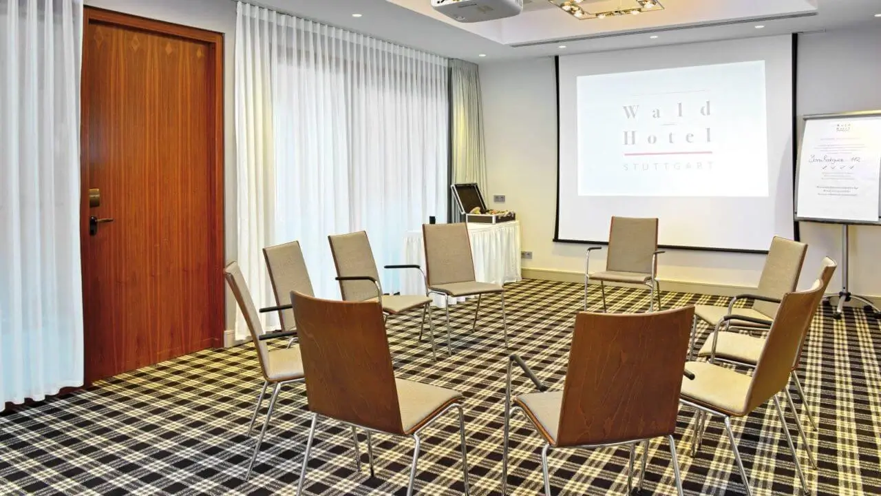 Ein heller Konferenzraum im Waldhotel Stuttgart mit Stühlen, die im Kreis angeordnet sind, einem Projektorbildschirm und einer Flipchart.