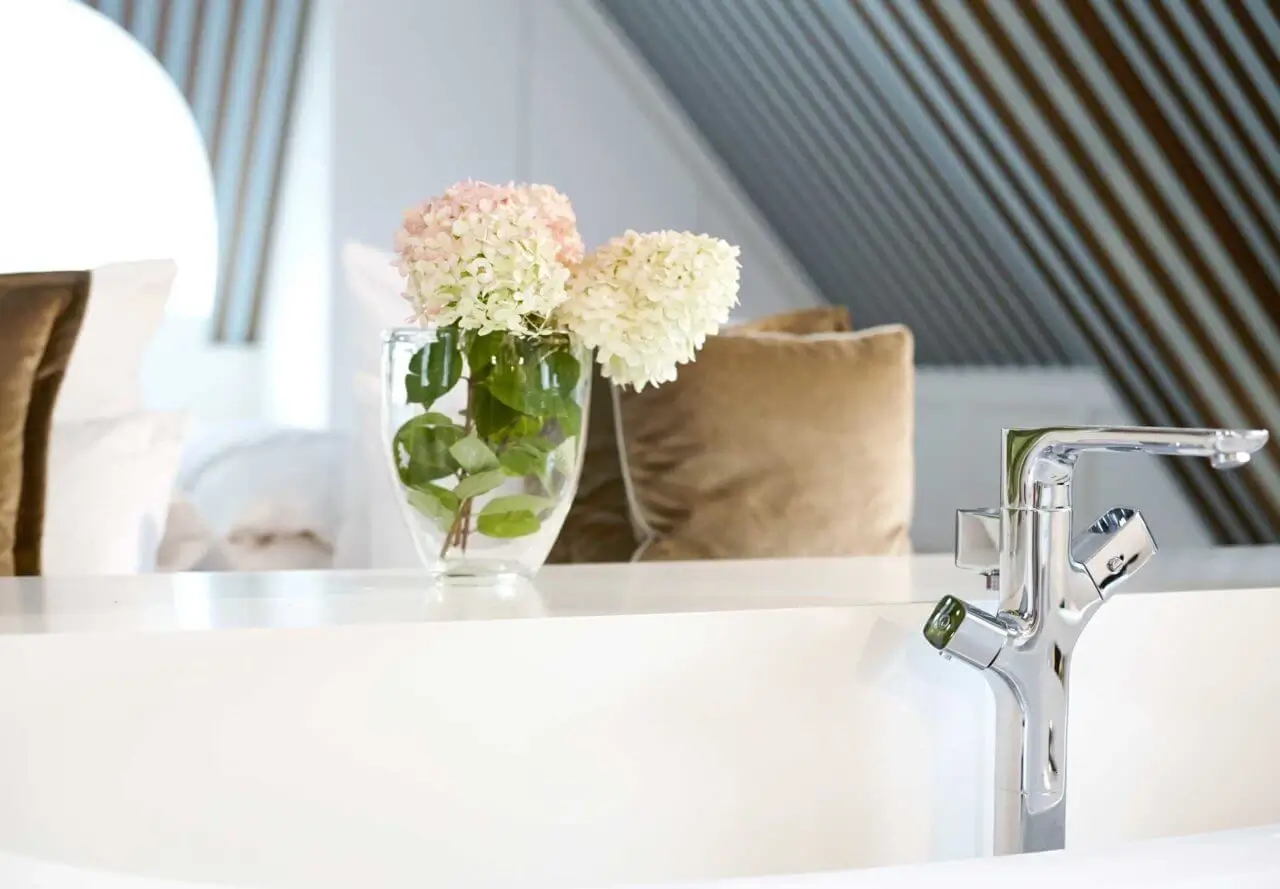 Nahaufnahme einer weißen Badewanne mit silbernen Armaturen und Blumen